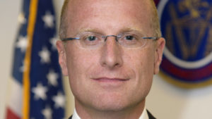 man in glasses standing in front of an american flag